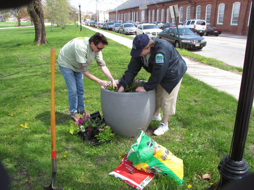 MDE employees Ray Bahr and Melissa Chatham plant flowers in a large outdoor flower pot on Earth Day 2009.